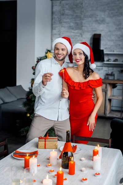 若いカップルで自宅ベンガル花火を楽しんでクリスマス帽子 — ストック写真