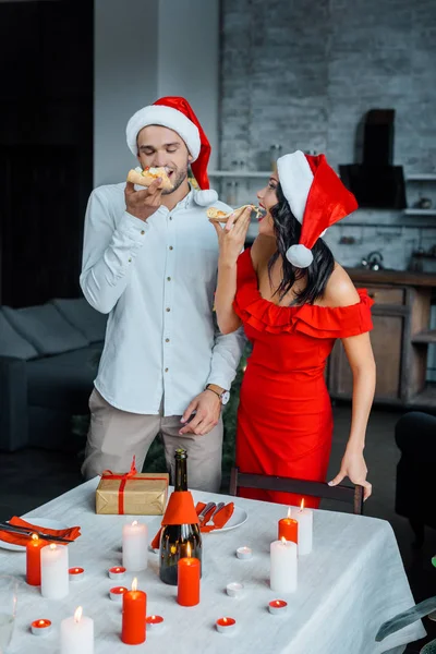 Heureux Jeune Couple Dans Chapeaux Noël Manger Pizza Près Table — Photo gratuite