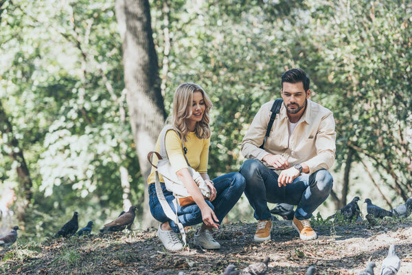 young couple with backpacks looking at pigeons in park