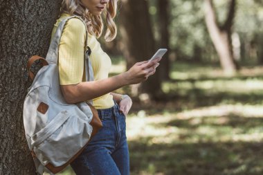 kadın ormanda smartphone kullanarak omuz sırt çantası ile kısmi görünümünü