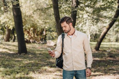 şık adam parkta smartphone kullanarak sırt çantası ile casual giyim
