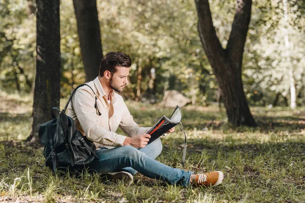 side view of traveler with map and backpack in park