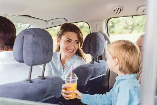 汽车旅行中给儿子送橙汁的女人 — 图库照片