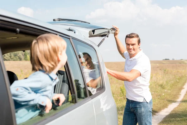 Little Son Looking Father Out Window While Opening Car Trunk — Free Stock Photo