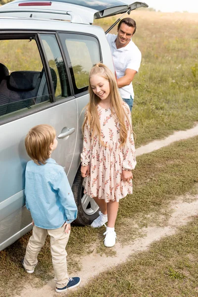 可爱的小孩子站在汽车旁边 而他们的父亲在外地打开树干在旅途中 — 免费的图库照片
