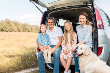 Genç aile araba bagajında oturan ve kamera alanında bakarak retriever köpek ile gülümseyen