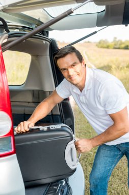 Bagajı alan otomobilin içine bavul paketleme ve kameraya bakarak yakışıklı adam