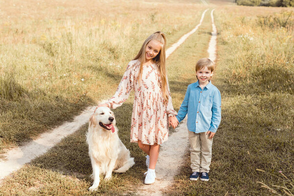 adorable little kids standing on road in field with golden retriever