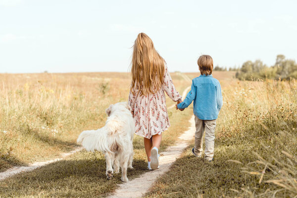 rear view little kids walking by road in field with golden retriever