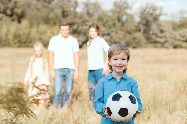 Pequeno Feliz Segurando Bola Enquanto Sua Família Embaçado Fundo Campo — Fotos gratuitas