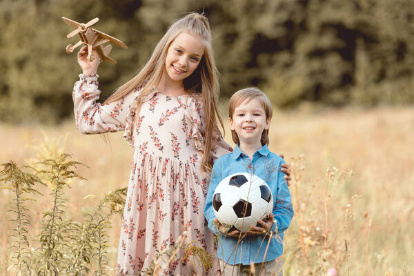 adorable little kids with toy airplane and football ball standing together in field