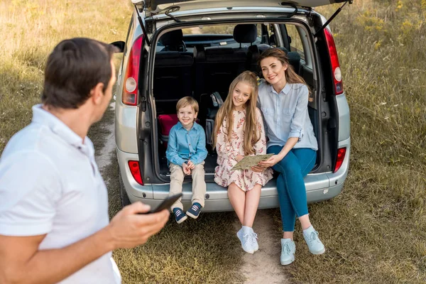 Man Using Smartphone While His Family Sitting Car Trunk Field — Stock Photo, Image