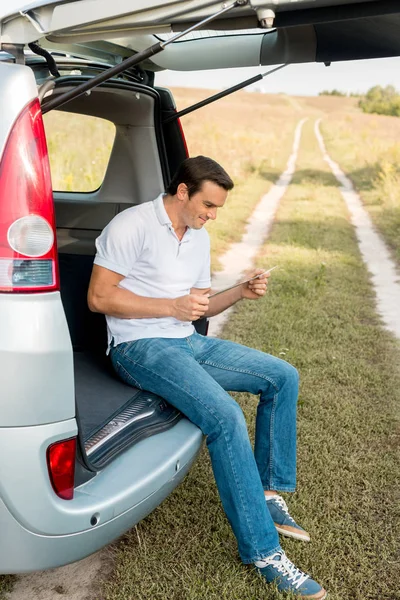 Handsome Smiling Man Sitting Car Trunk Looking Map Field — Free Stock Photo