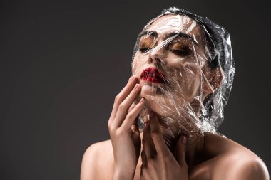 sensual woman with face wrapped in transparent cellophane with drops isolated on black  clipart