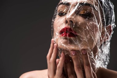 sensual young woman with face wrapped in wet transparent cellophane isolated on black  clipart