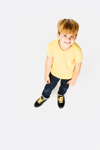 high angle view of adorable happy little boy standing and smiling at camera isolated on white