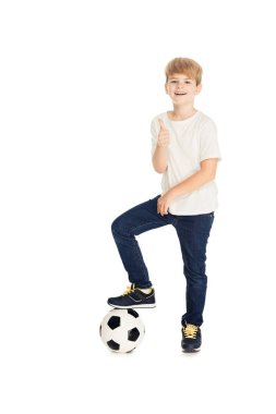 bacak üzerinde futbol topu koyarak ve izole üzerinde beyaz yukarı gösteren gülümseyen sevimli çocuk