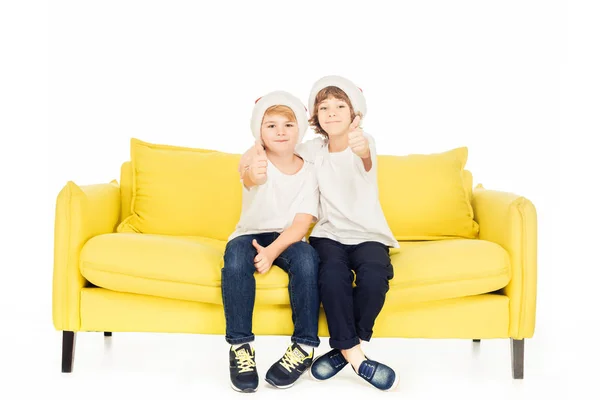 Adorável Meninos Santa Chapéus Sentado Sofá Amarelo Isolado Branco Mostrando — Fotografia de Stock Grátis