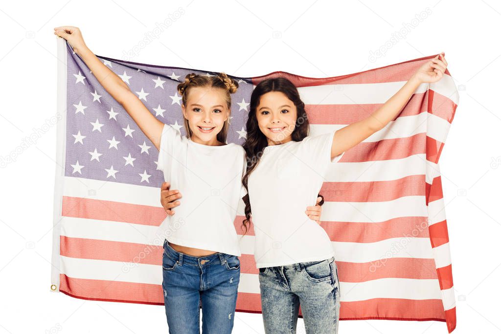 cheerful adorable kids standing under american flag and looking at camera isolated on white