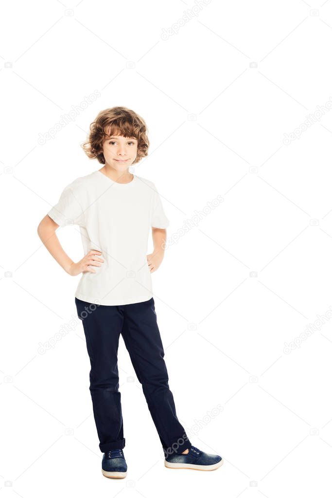 smiling adorable boy standing with hands akimbo and looking at camera isolated on white