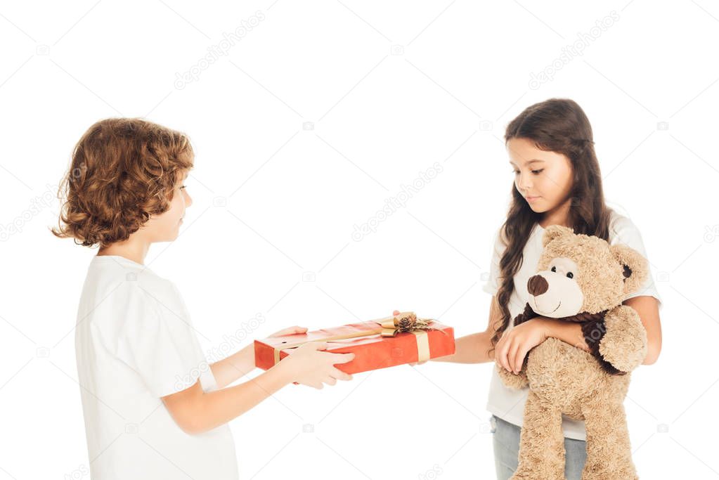 side view of boy presenting gift box to friend isolated on white
