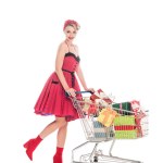 Attractive pin up woman carrying shopping cart with pile of gift boxes isolated on white