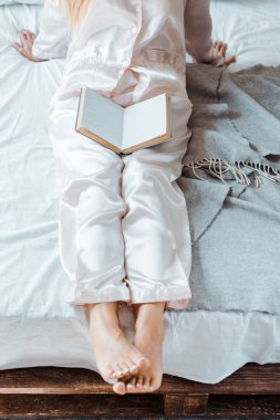 Genç kadın yatakta kitap ile oturan pijama kadeh kırpılmış