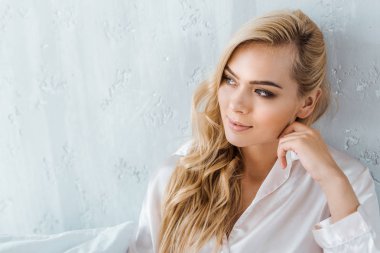 güzel gülümseyen genç sarışın kadın yatakta oturmuş ve uzağa bakarak pijama