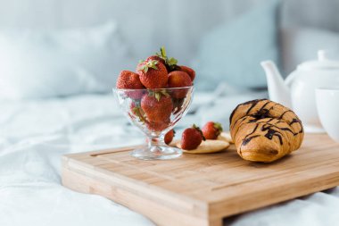 yummy breakfast of strawberries and croissant on wooden tray on bed clipart