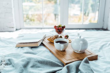 appetizing breakfast and open book on bed in bedroom clipart