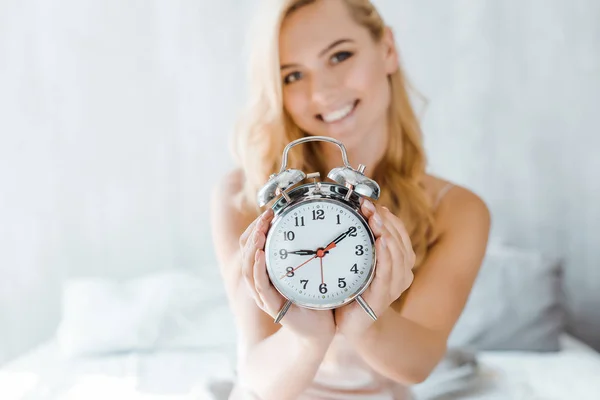 目覚まし時計を押し 寝室でカメラで笑顔の美しい若い女性のクローズ アップ ビュー — ストック写真