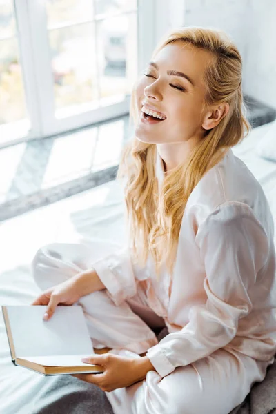 Happy Blonde Girl Pajamas Laughing While Sitting Bed Book — Stock Photo, Image