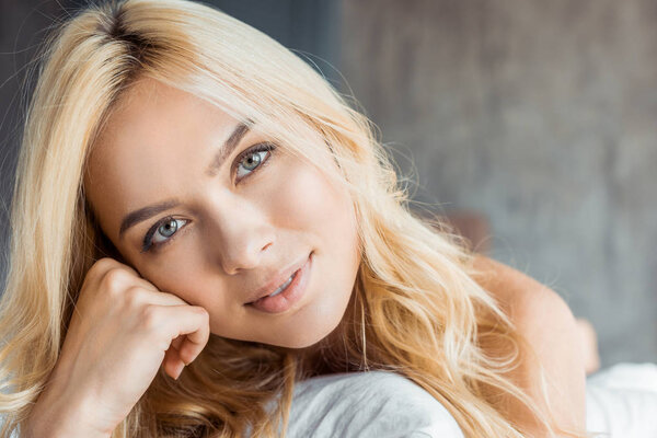 headshot of attractive blonde woman lying in bedroom and looking at camera