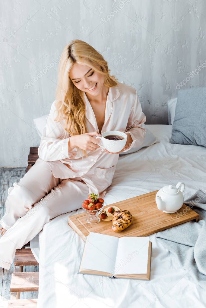 high angle view of beautiful smiling woman holding cup of tea in bed in morning