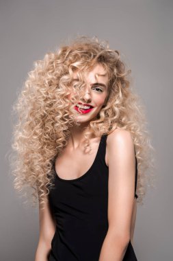 portrait of beautiful young woman with long curly hair smiling at camera isolated on grey