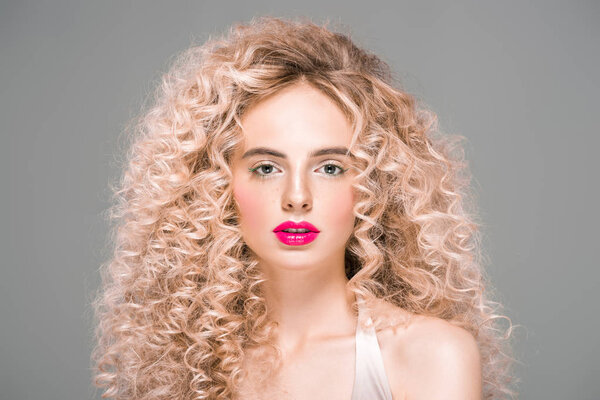 portrait of attractive young woman with long curly hair looking at camera isolated on grey 