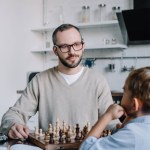 Far i glasögon tittar på lille son medan du spelar schack tillsammans hemma