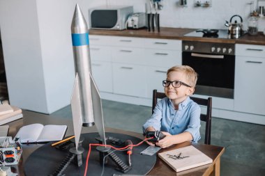 adorable boy sitting at table and testing rocket model in kitchen on weekend clipart