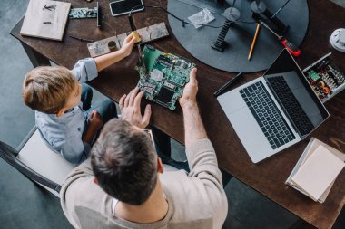 overhead view of father and son soldering circuit board with soldering iron at home clipart