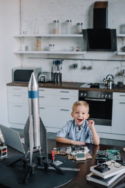 mutfak ve kameraya bakarak roket modeli ile masada oturan mutlu sevimli çocuk