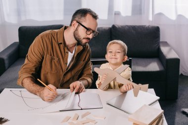 father in eyeglasses and cute little son modeling plane together at home clipart