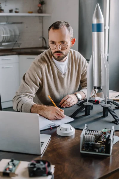 Stilig Ingenjör Modellera Raket Tittar Laptop Och Göra Anteckningar Hemma — Stockfoto