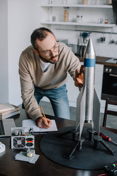 handsome engineer modeling and measuring rocket at home