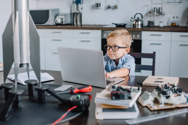 有趣的可爱的男孩使用笔记本电脑在桌子上的火箭模型在厨房上周末 — 图库照片