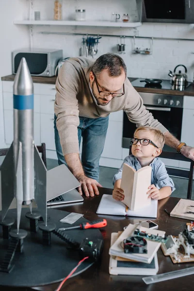 father and son modeling rocket and looking at each other at home