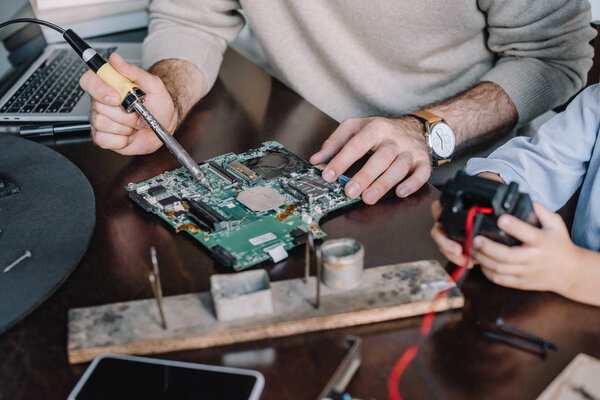 cropped image of father and son soldering circuit board with soldering iron at home