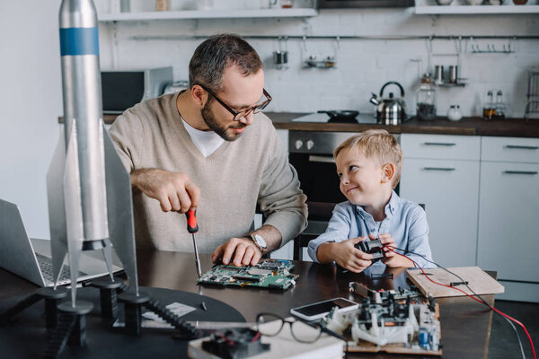 cheerful father and son repairing circuit board and looking at each other at home