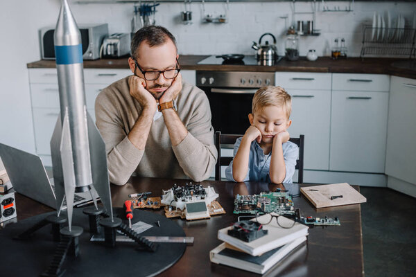 pensive father and son looking at circuit board on table at home