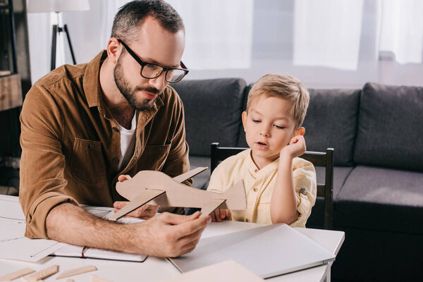father in eyeglasses and adorable little boy modeling wooden plane together
