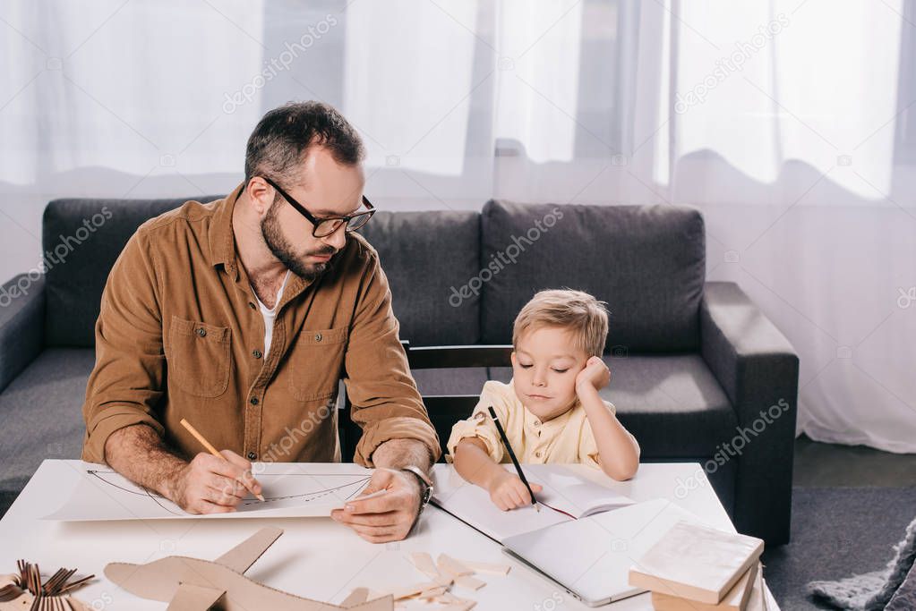 father and little son drawing while modeling plane together at home 